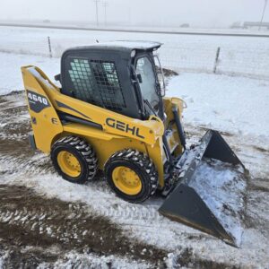 Angled view of a Gehl 4640 skid steer loader, showing its protective cab, tires with snow grip, and bucket attachment. Perfect for farming and construction use in Western Canada