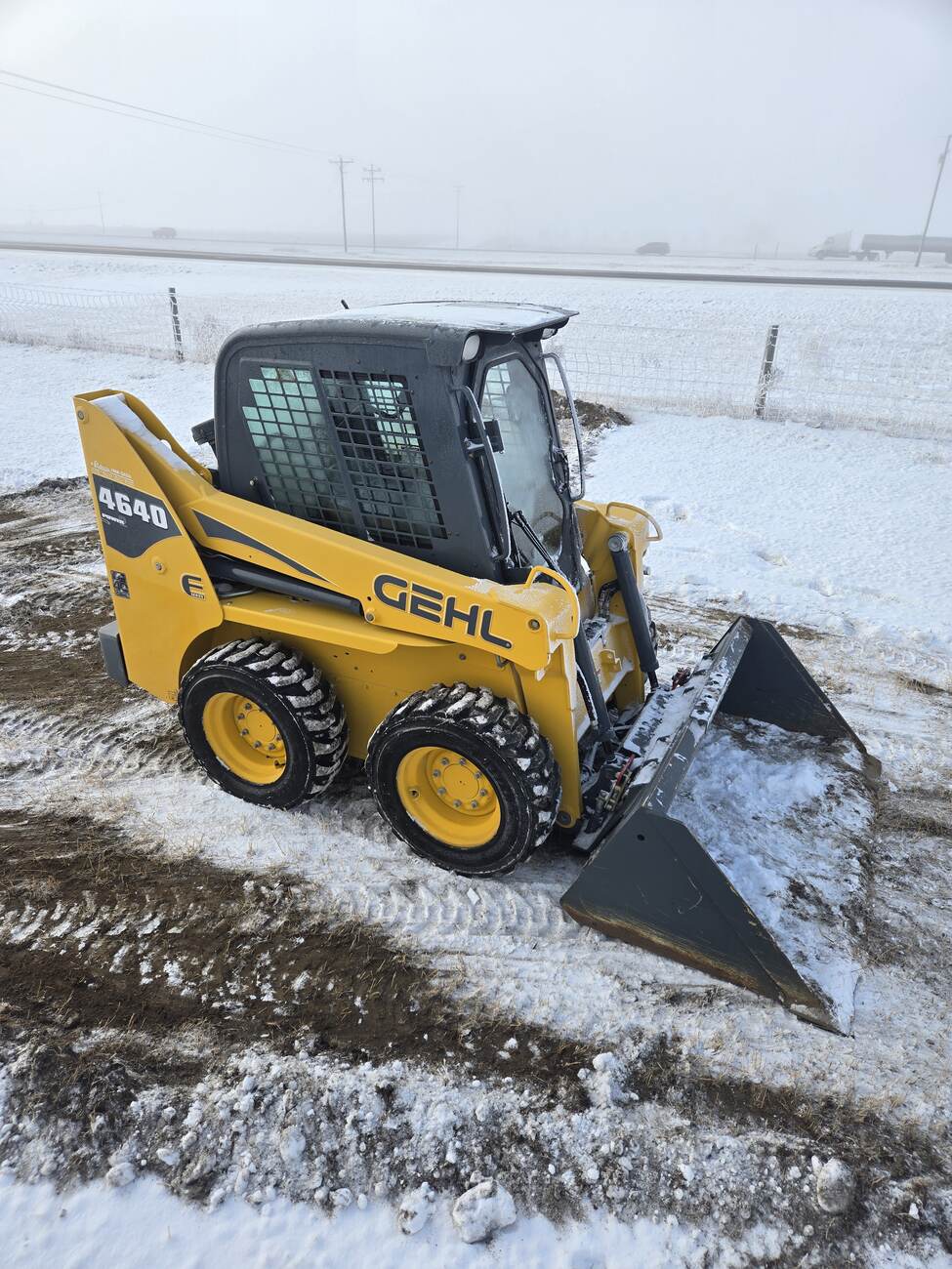 Angled view of a Gehl 4640 skid steer loader, showing its protective cab, tires with snow grip, and bucket attachment. Perfect for farming and construction use in Western Canada