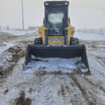 Front-facing image of a Gehl 4640 skid steer loader with snow-covered windows and a bucket attachment. Ideal for buyers looking for a reliable compact loader in Western Canada