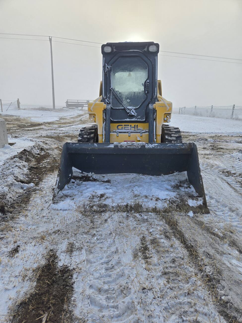 Front-facing image of a Gehl 4640 skid steer loader with snow-covered windows and a bucket attachment. Ideal for buyers looking for a reliable compact loader in Western Canada