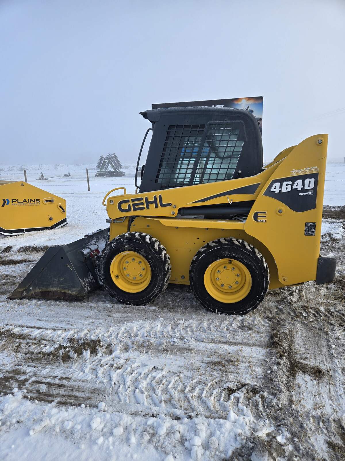 Full side profile of a Gehl 4640 skid steer loader designed for efficient material handling and construction work For sale in Western Canada arctic snow pusher in background