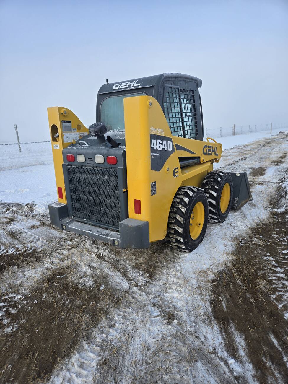 Rear side perspective of a Gehl 4640 skid steer loader on a snowy worksite. Equipped with durable tires and a compact frame, ideal for heavy-duty tasks in Western Canada.jpg