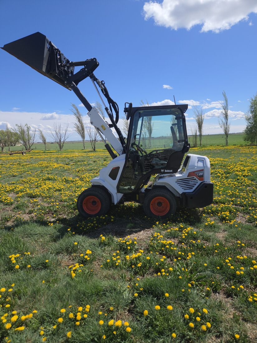 2022-bobcat-l28-small-articulated-loader-for-sale-western-canada-lifted-bucket-side-view-field