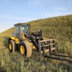 John Deere 524K-II loader with pallet forks attachment in tall grass, Plains Equipment Rentals for sale