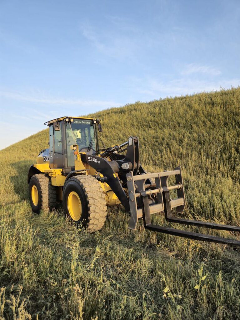 John Deere 524K-II loader with pallet forks attachment in tall grass, Plains Equipment Rentals for sale