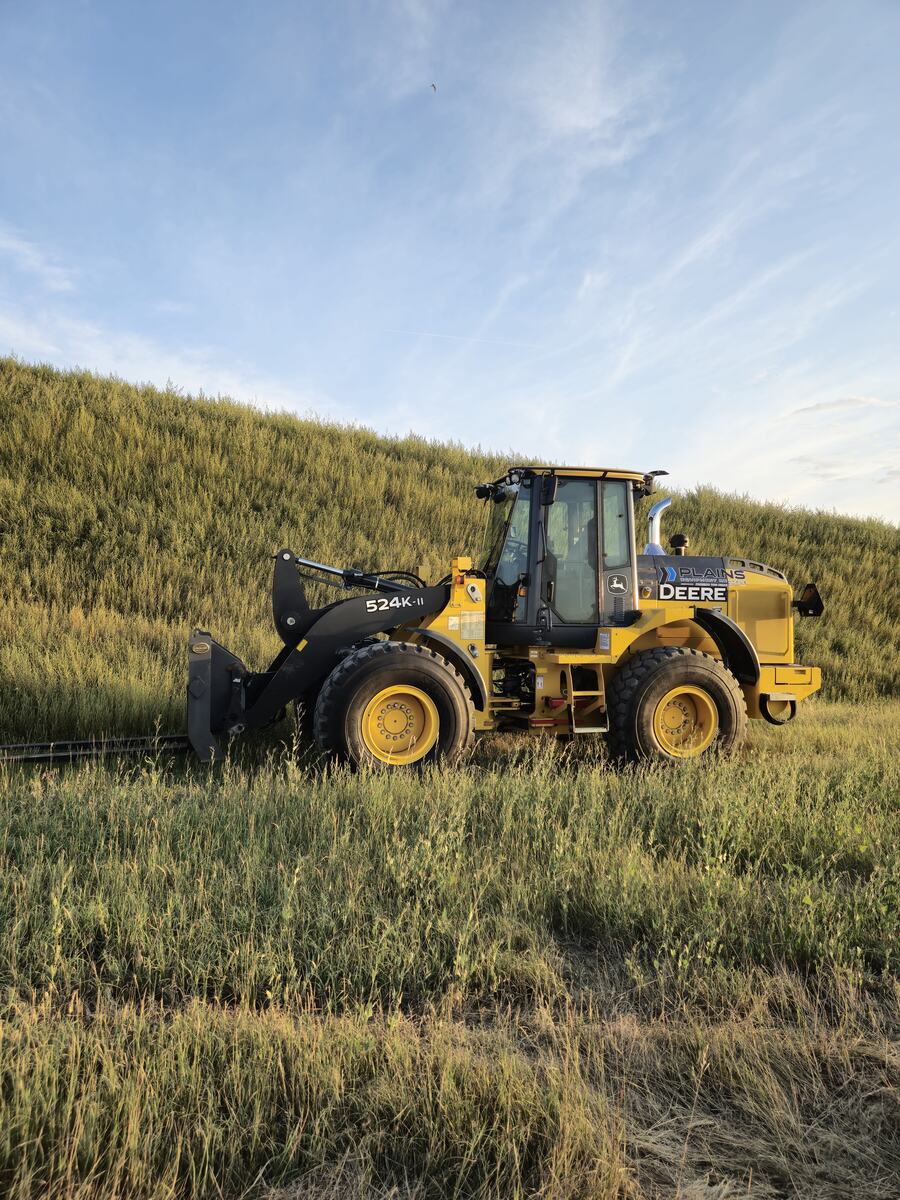 John Deere 524K-II wheel loader with pallet forks from Plains Equipment Rentals in Western Canada for sale, side view in field