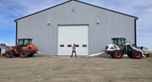 Two heavy equipment loaders demonstrating cable strength outside industrial warehouse building