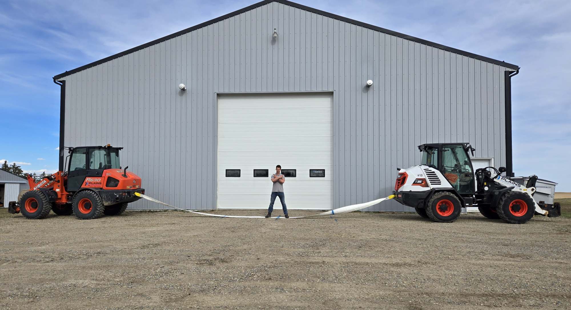 Two heavy equipment loaders demonstrating cable strength outside industrial warehouse building