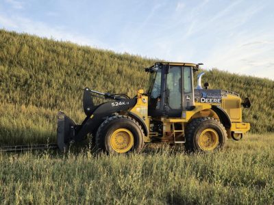 John Deere 524K-II wheel loader with pallet forks from Plains Equipment Rentals in Western Canada for sale, side view in field